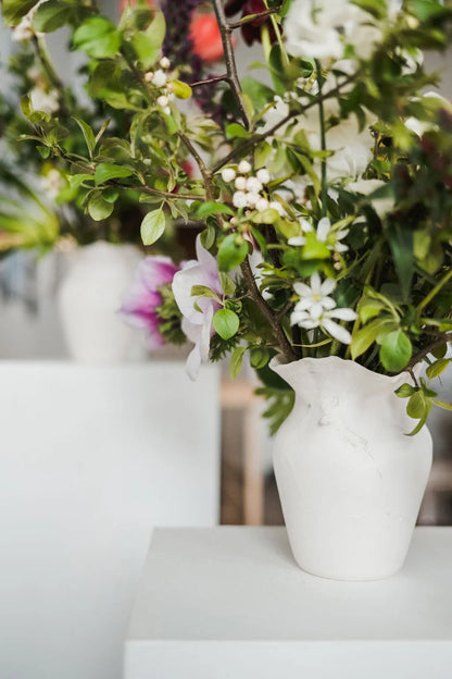 White vase with greenery and flowers on a white surface