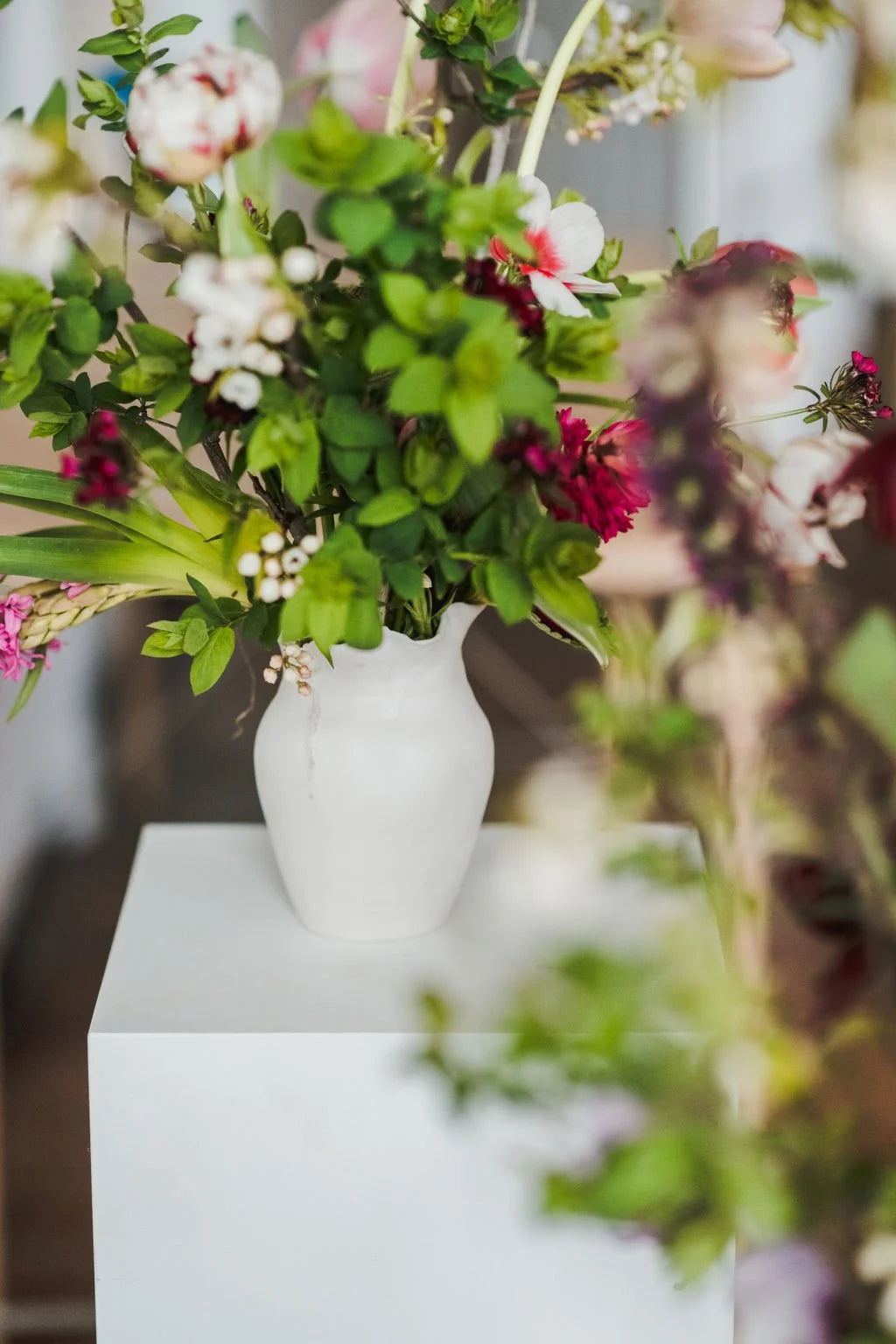 White vase with flowers on a white pedestal against a blurred floral background