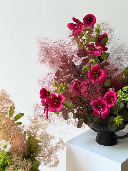 Bouquet of pink flowers in a black vase on a white surface with a white background