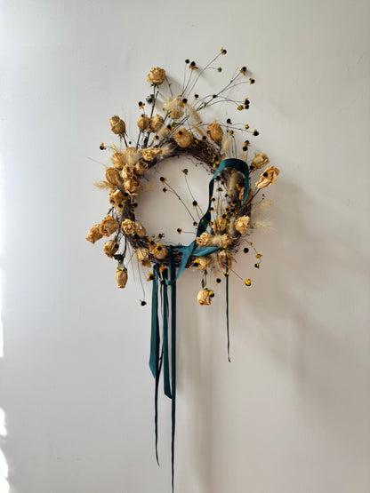 Decorative wreath with dried flowers and ribbons on a white wall