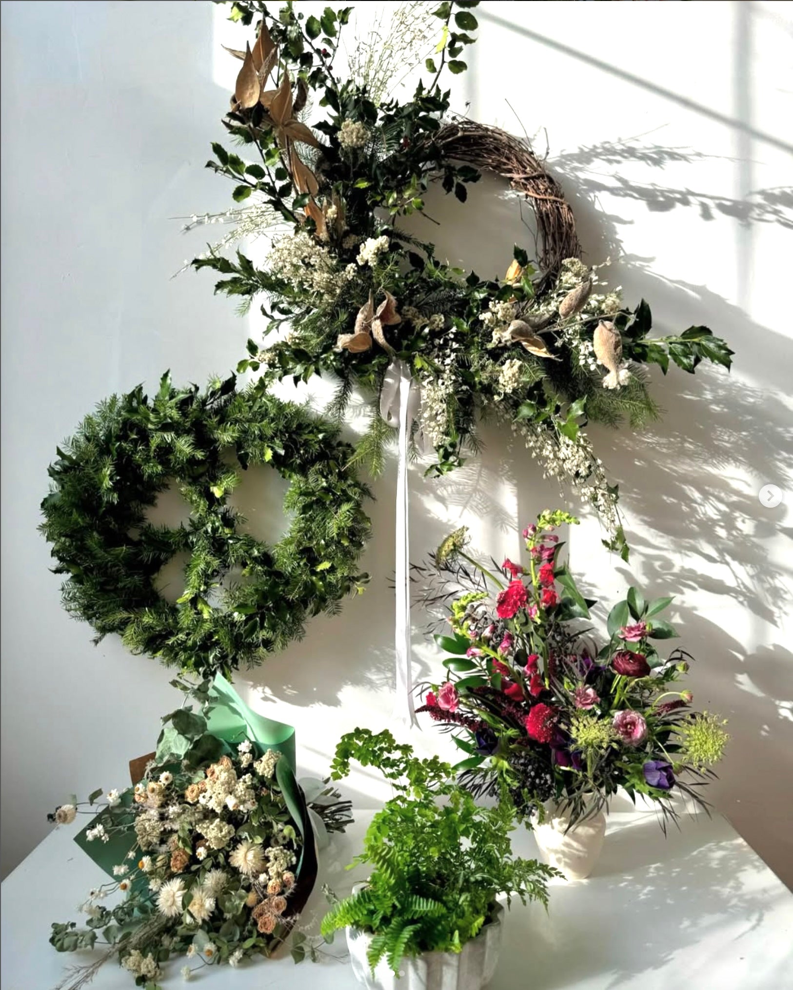 Collection of floral arrangements and wreaths on a white surface with a light background
