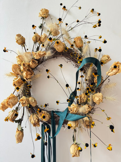 Decorative wreath with dried flowers and a blue ribbon on a white background