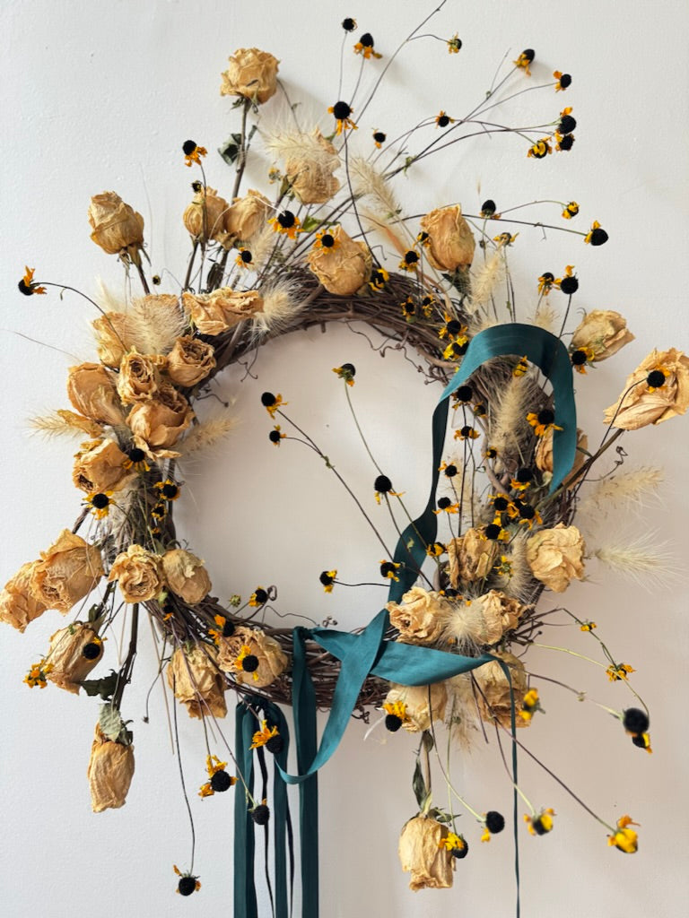 Decorative wreath with dried flowers and a blue ribbon on a white background