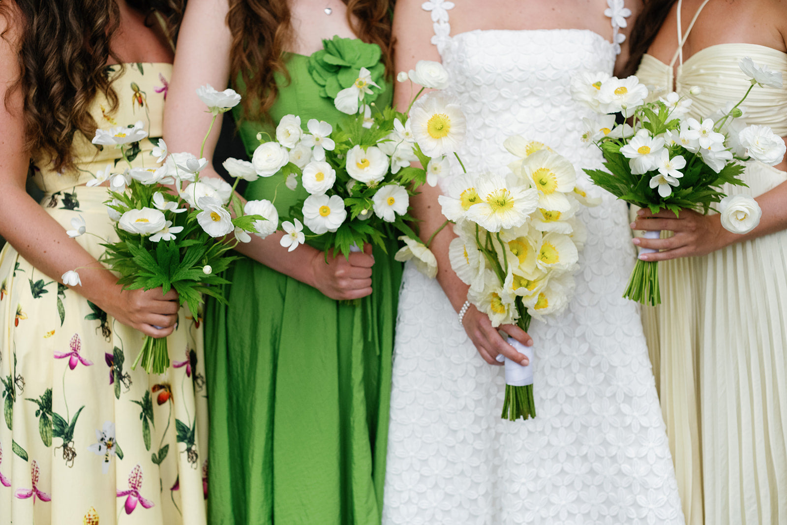 Bride in a white dress with bridesmaids in green and cream dresses holding all white floral bouquets.