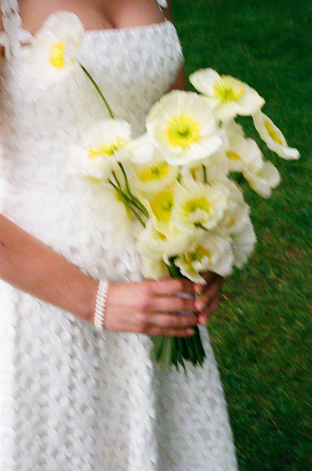 Bride holding a bouquet of white flowers with green grass in the background