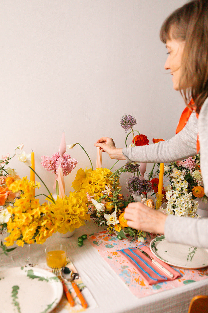 Woman arranging flowers on a table with colorful candles and tableware.