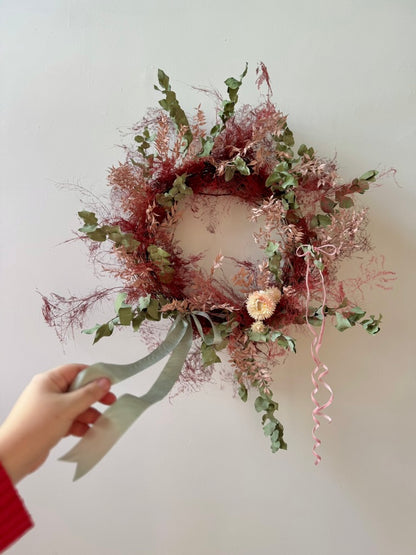 Decorative wreath with flowers and ribbons held by a hand against a plain background