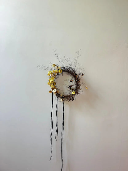 Decorative wreath with yellow flowers and black ribbons on a plain wall