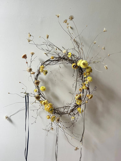 Decorative wreath with yellow flowers and dried elements on a plain background