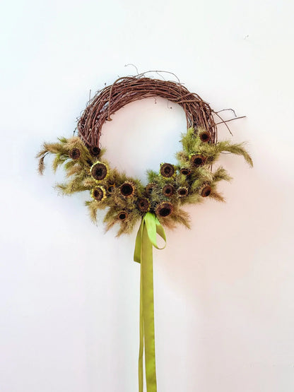 Wreath with sunflower-like flowers and a green ribbon on a white background