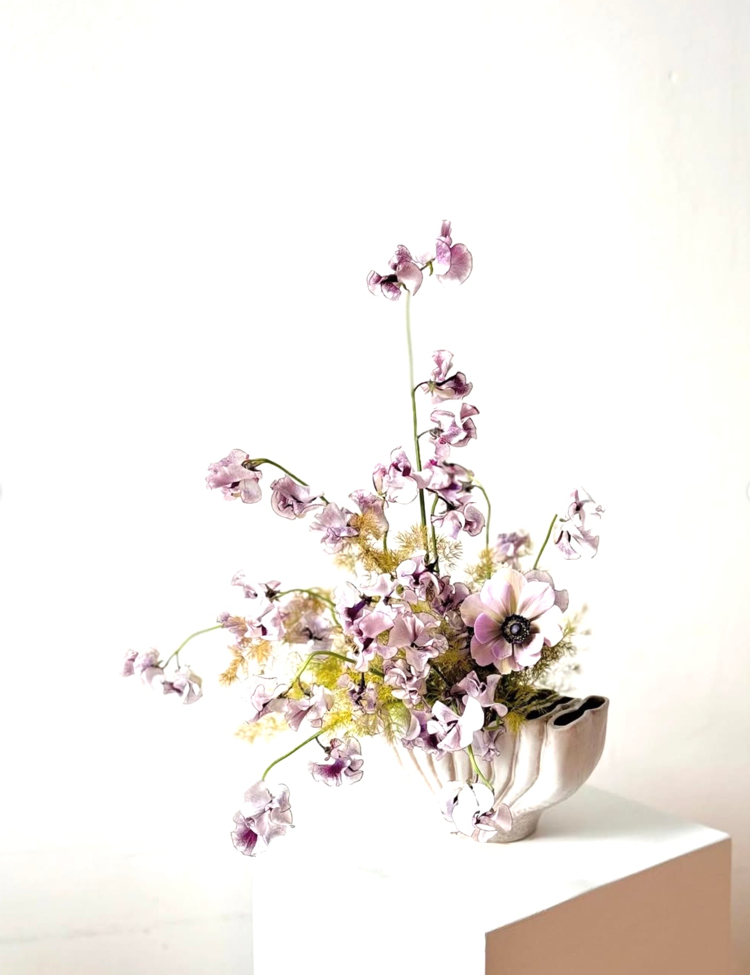 Floral arrangement in a modern white vase on a light surface with a white background