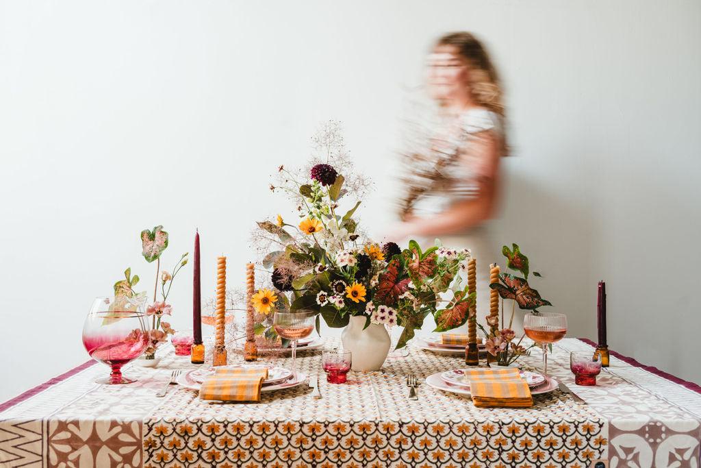 Decorated table with flowers, candles, and glasses, blurred person in the background