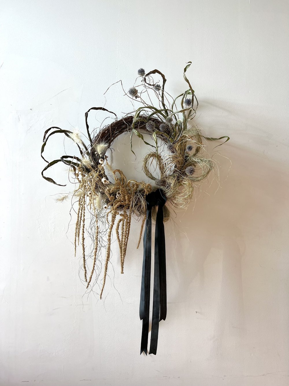 Decorative wreath with natural elements and a black ribbon on a white background