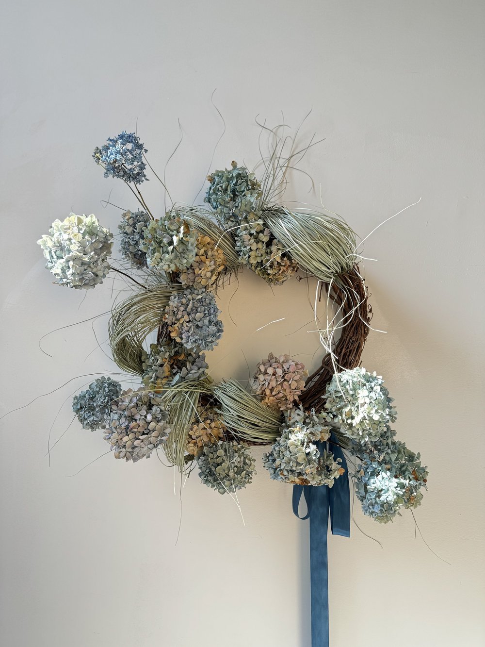 Decorative wreath with flowers and a blue ribbon on a plain background