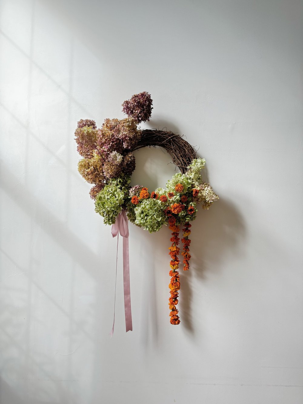 Decorative wreath with flowers and ribbons on a white wall