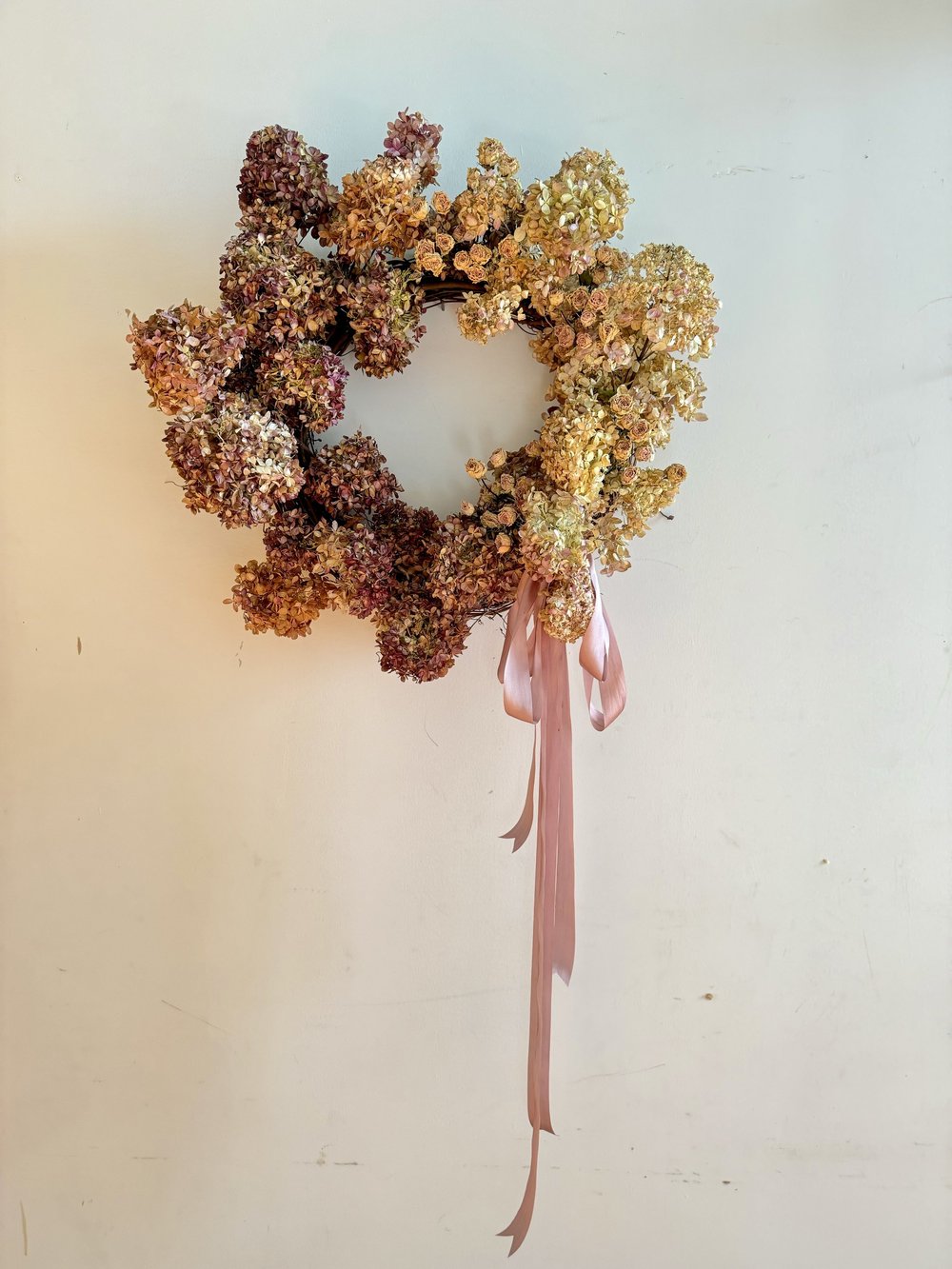 Wreath with dried flowers and a pink ribbon on a light background
