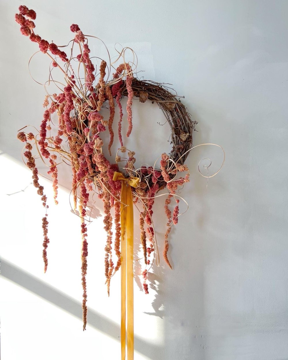 Decorative wreath with dried flowers and a yellow ribbon on a white wall