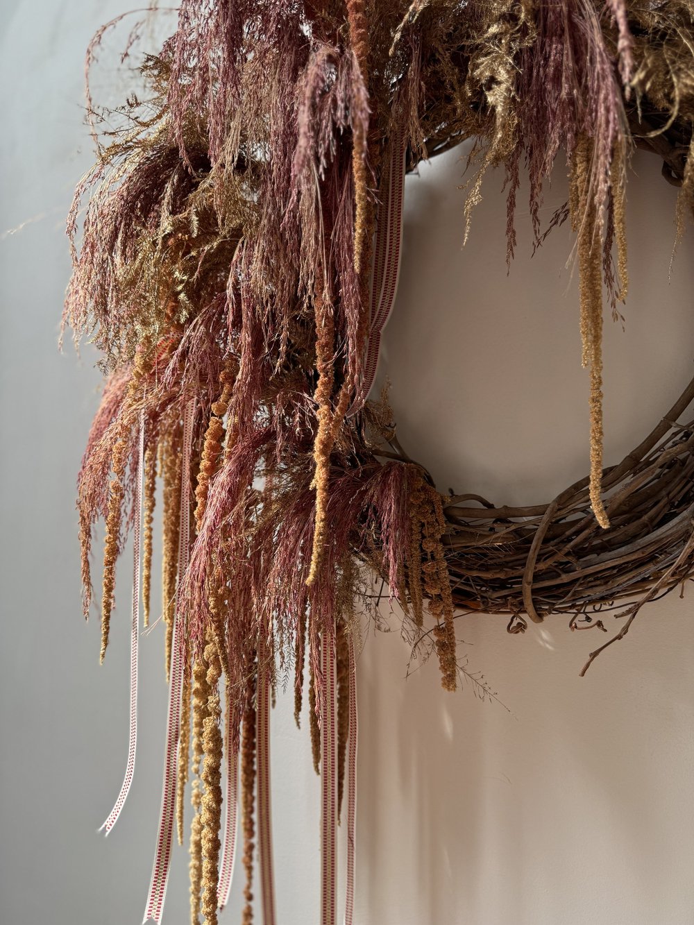 Decorative wreath with dried grasses and ribbons on a neutral background