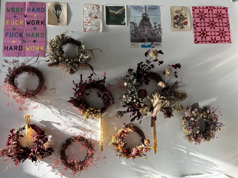Collection of dried flower wreaths on a white surface with decorative posters in the background.
