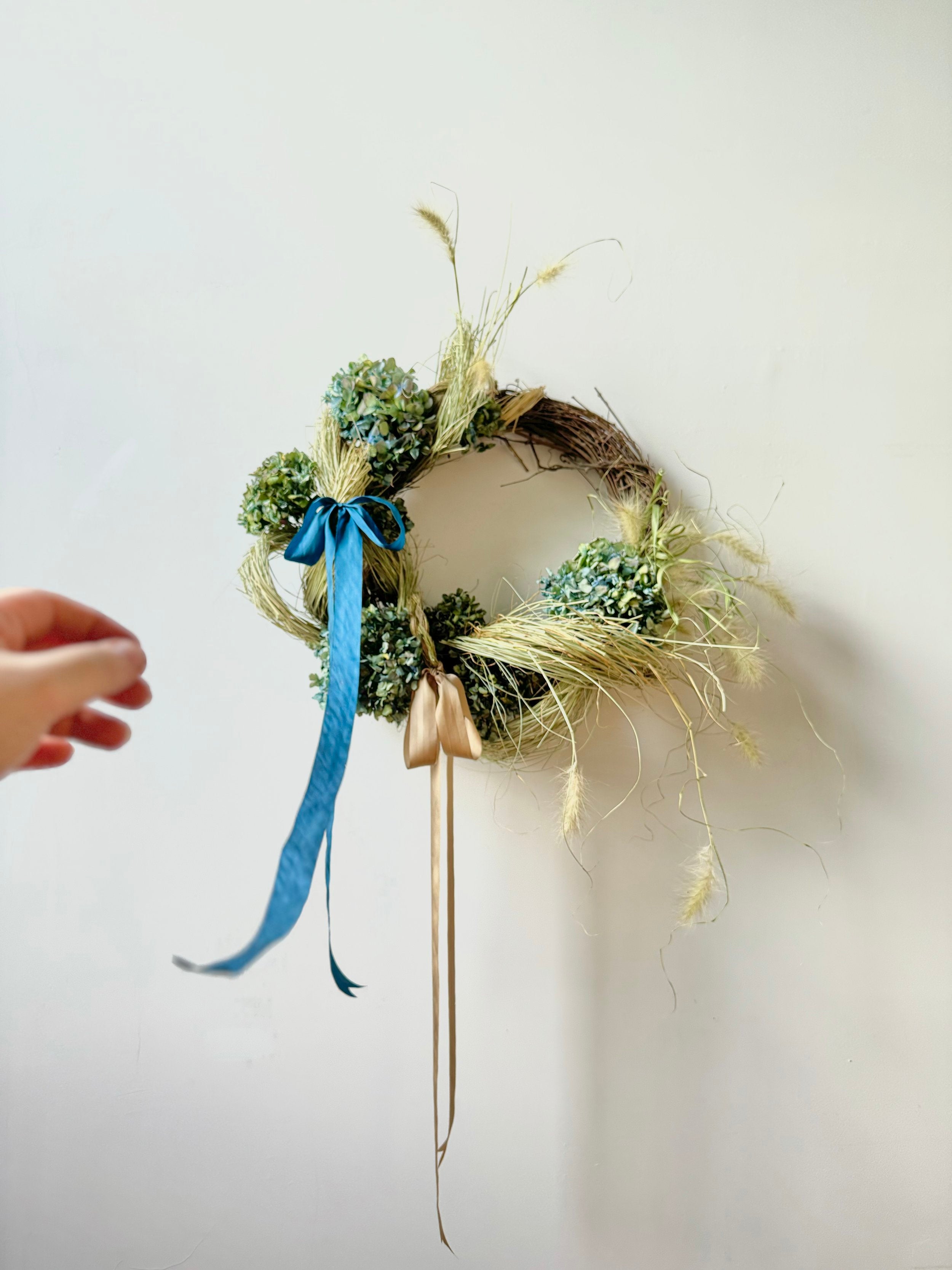 Decorative wreath with greenery and a blue ribbon on a white wall