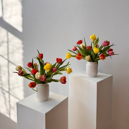For flower delivery in portland maine small white vases with colorful tulips on white pedestals against a light gray wall
