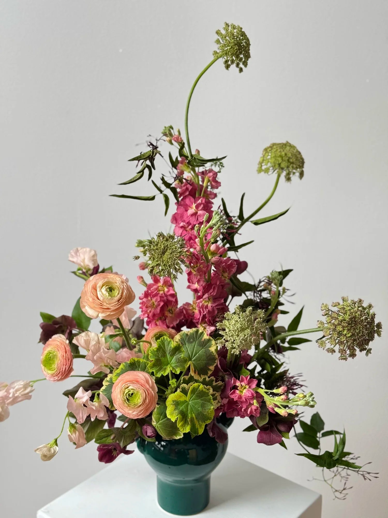Floral arrangement in a green vase on a white surface with a light gray background