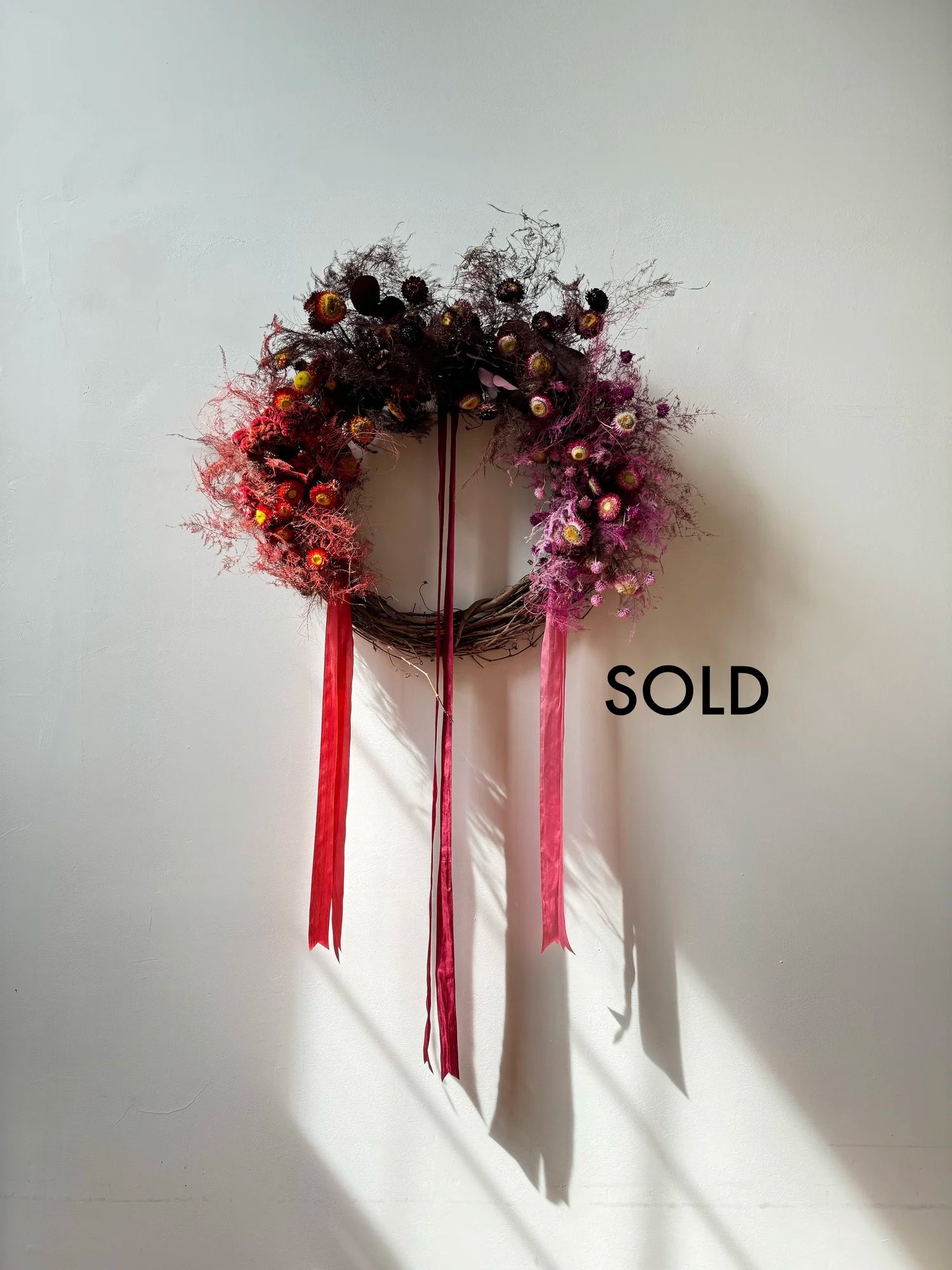 Decorative wreath with red ribbons on a white wall, with 'SOLD' text.