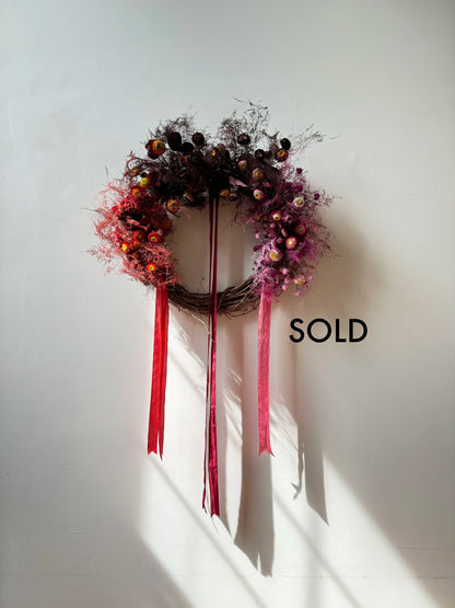 Decorative wreath with red ribbons on a white wall, with 'SOLD' text.