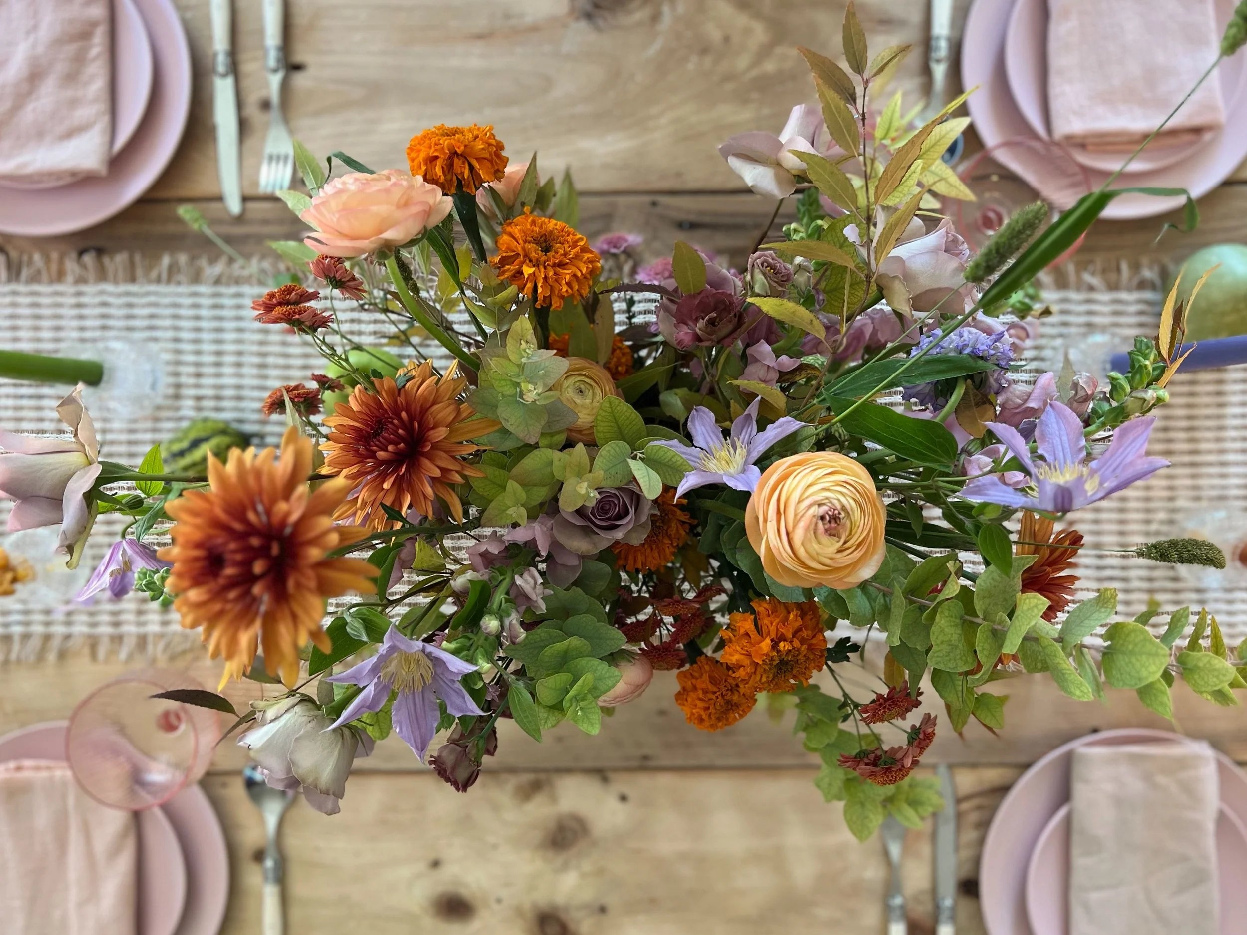 Colorful flower arrangement on a wooden table with pink plates and napkins.