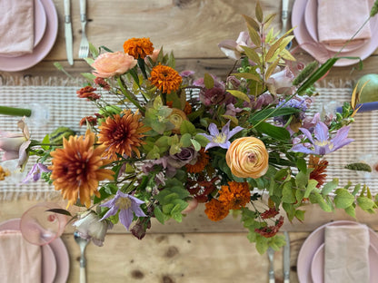 Colorful flower arrangement on a wooden table with pink plates and napkins.