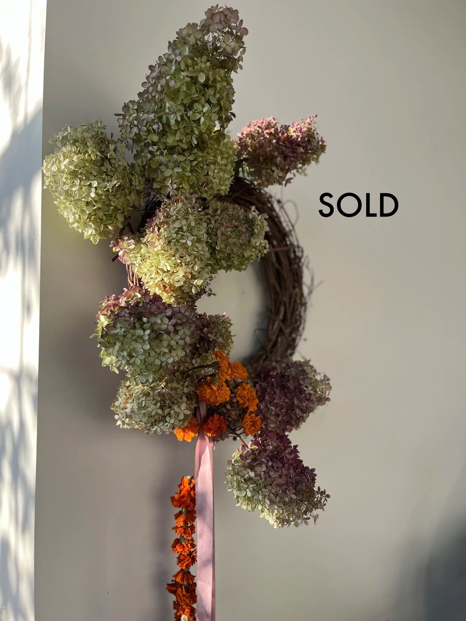 Decorative wreath with green and purple flowers and orange accents on a plain background.