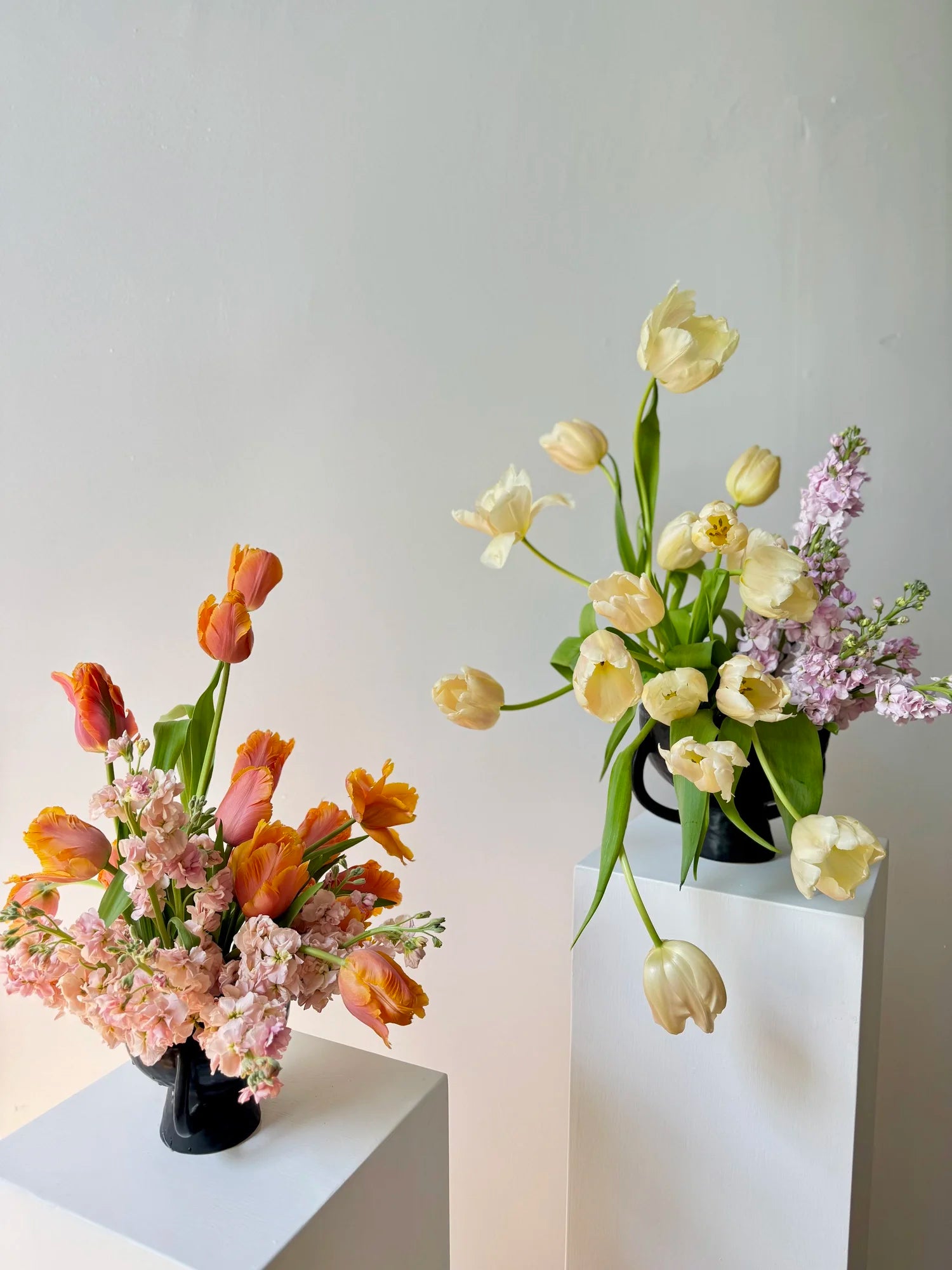 Two flower arrangements on white surfaces against a light gray background