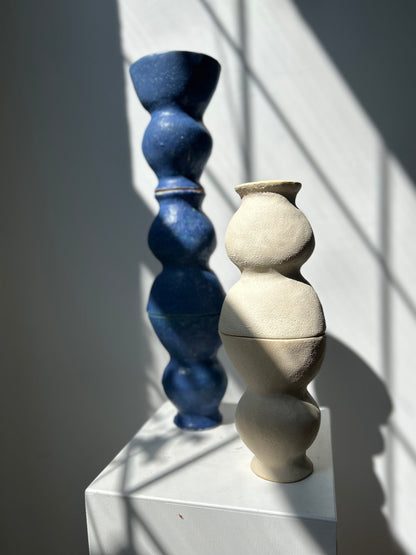 Two ceramic vases, one blue and one beige, on a white surface with a light gray background.
