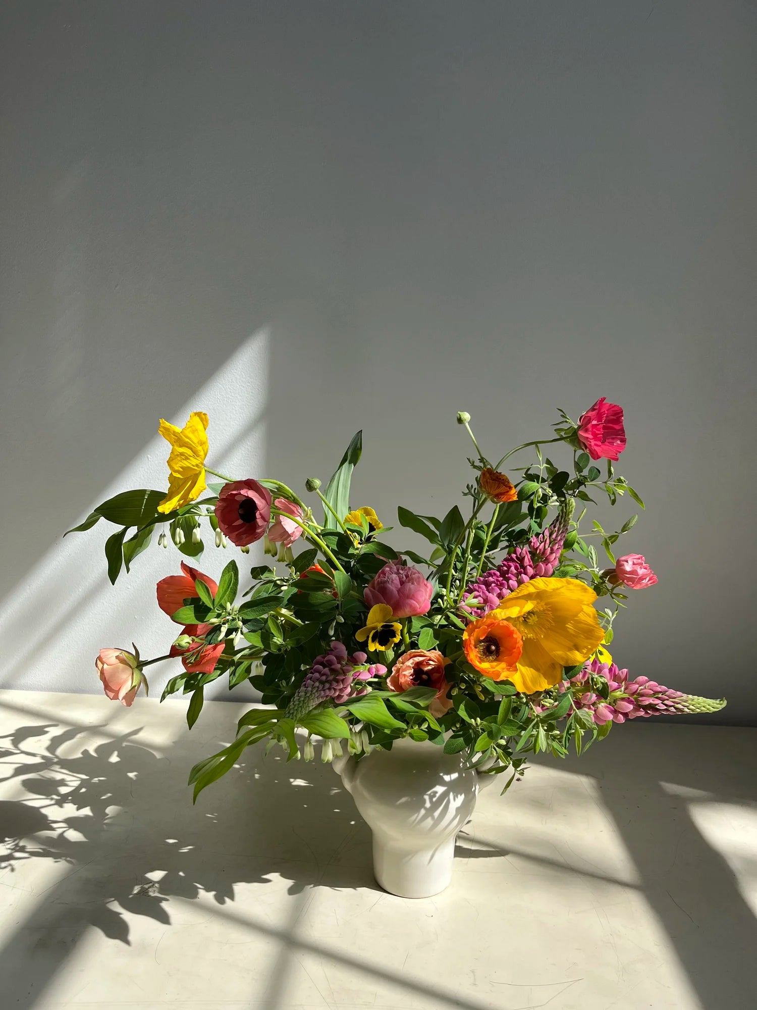 Bouquet of colorful flowers in a white vase on a light surface with a gray background