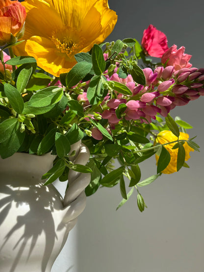 Bouquet of flowers including yellow, pink, and green in a white vase.