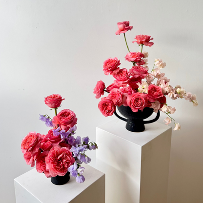 Two flower arrangements on white pedestals against a light gray background
