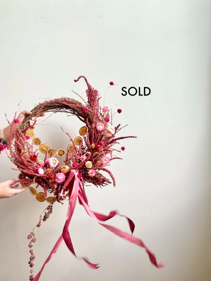 Decorative wreath with pink ribbons and beads on a plain background, with 'SOLD' text.
