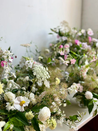 Close-up of a floral arrangement with white, pink, and green flowers on a white background.