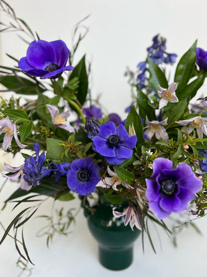 Bouquet of purple flowers with green leaves in a dark green vase on a white background