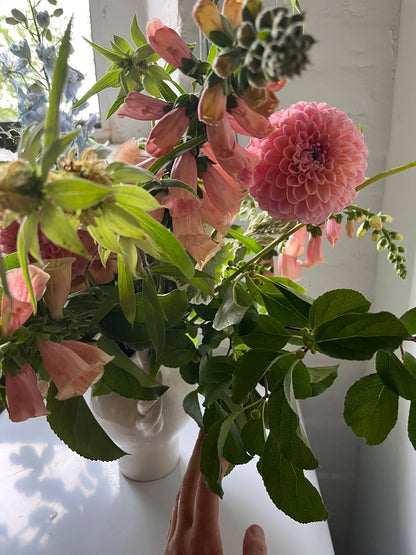 Bouquet of pink flowers with green leaves in a white vase on a light surface.
