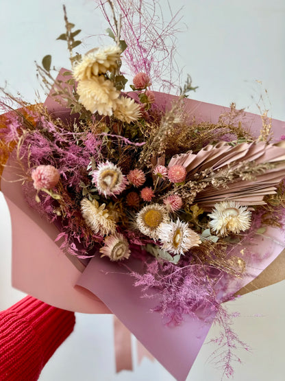 Bouquet of dried flowers wrapped in pink paper held by a person wearing red gloves.