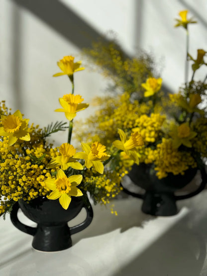 Yellow flowers in black vases on a white surface