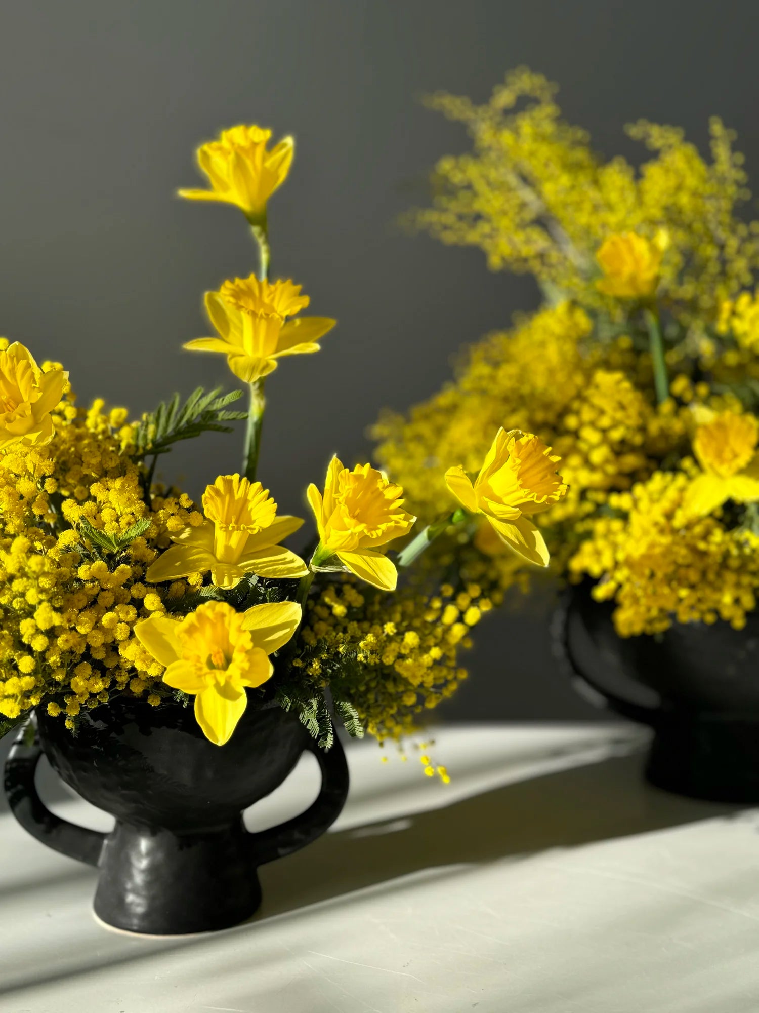 Two black urns filled with yellow flowers on a gray background