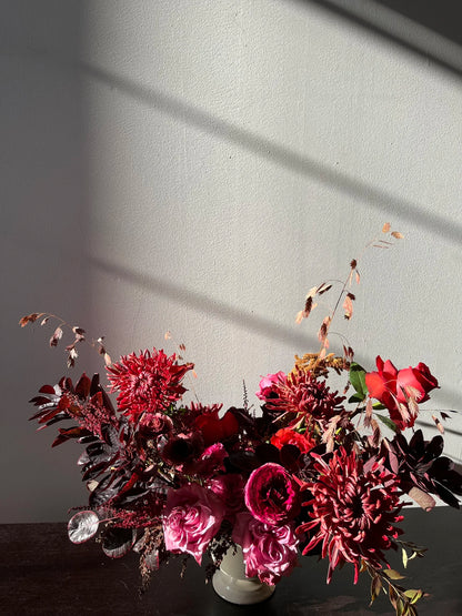 Bouquet of red and pink flowers with green leaves on a dark surface against a light gray wall.