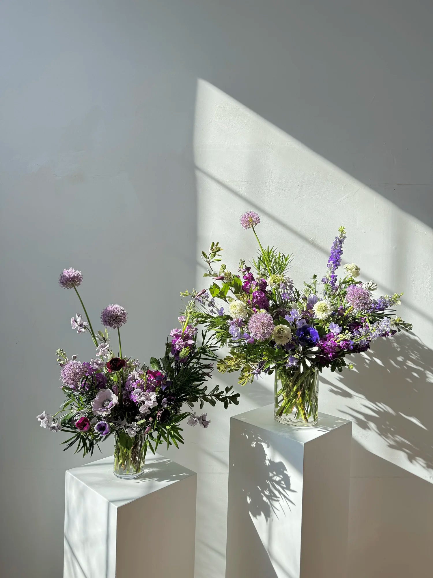 Two flower bouquets on white pedestals against a light gray wall.