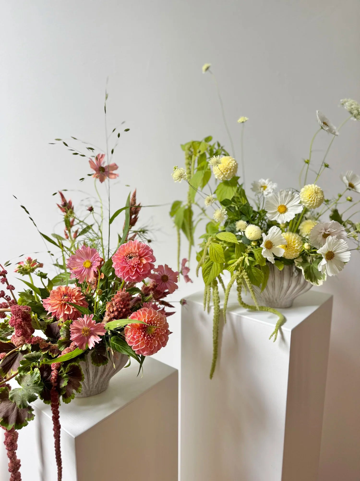Two floral arrangements on white pedestals against a light gray background