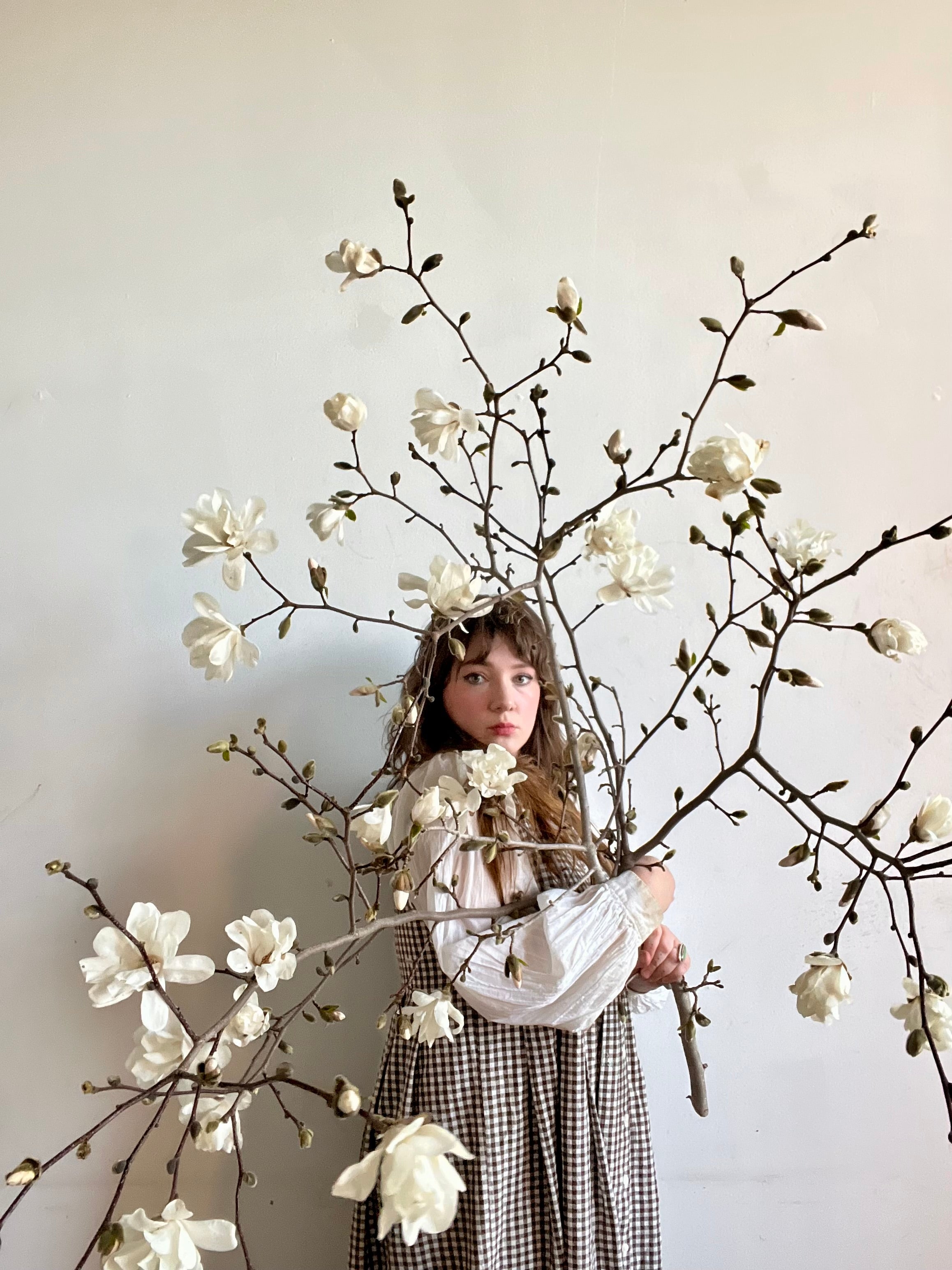 Maine florist holding large blooming magnolia branches while looking at the camera on a white background.