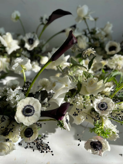 Close-up of a bouquet of white and black flowers with green leaves on a light background