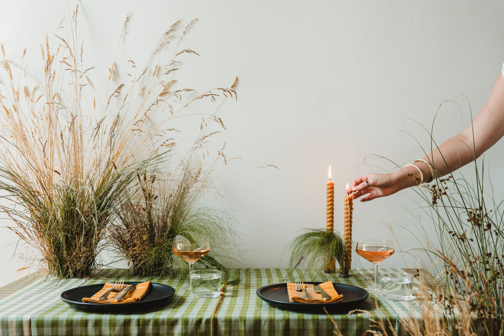 Dining table setting with candles, plates, and glasses on a checkered tablecloth.