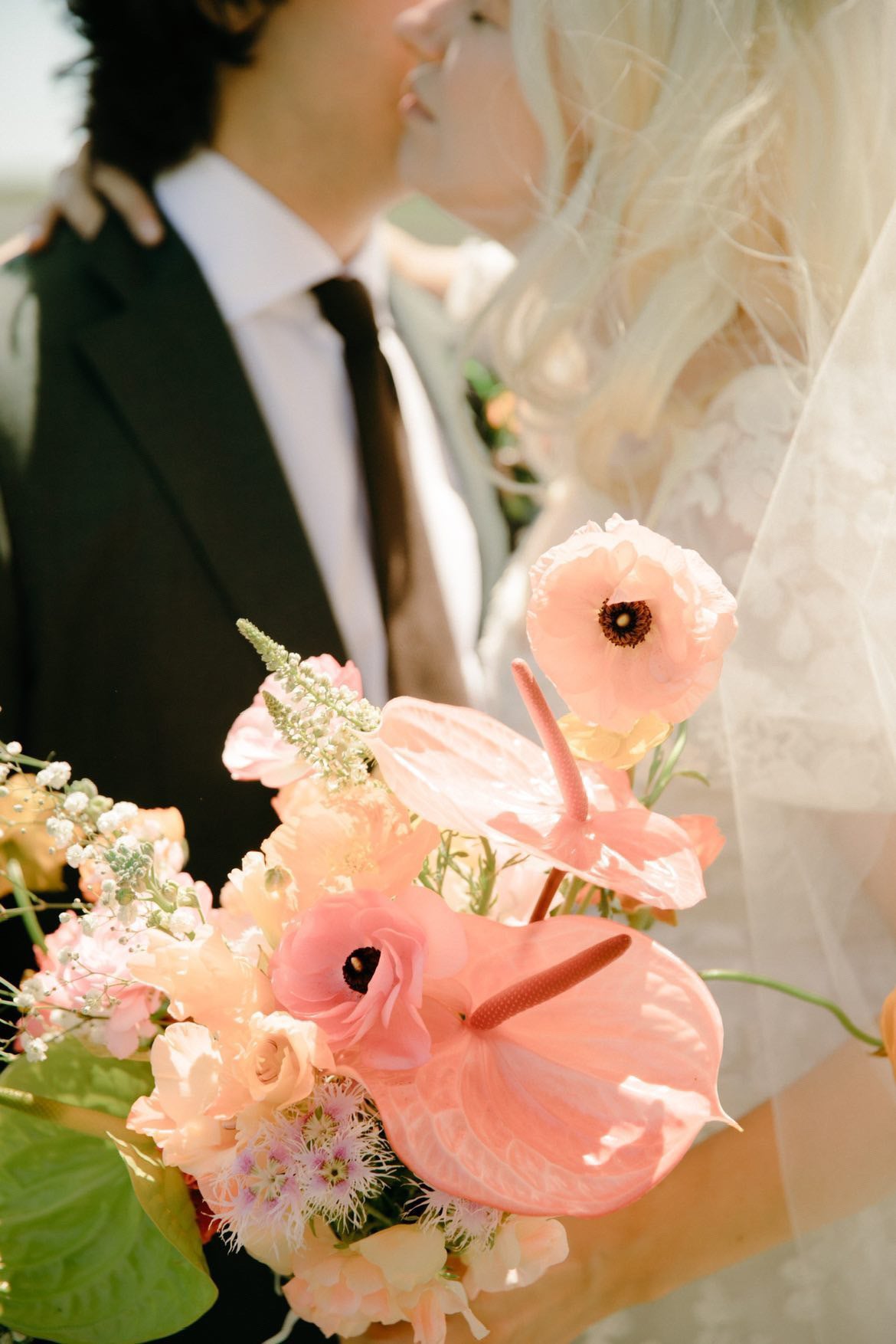Close-up of a bouquet with pink flowers and green leaves, featuring a couple in the background.